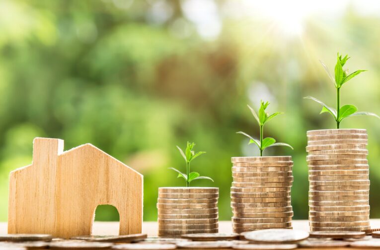 photo showing a table with a wood house, coins and nature displaying how to create wealth investing in real estate