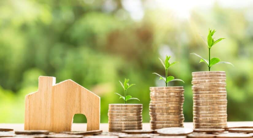 photo showing a table with a wood house, coins and nature displaying how to create wealth investing in real estate