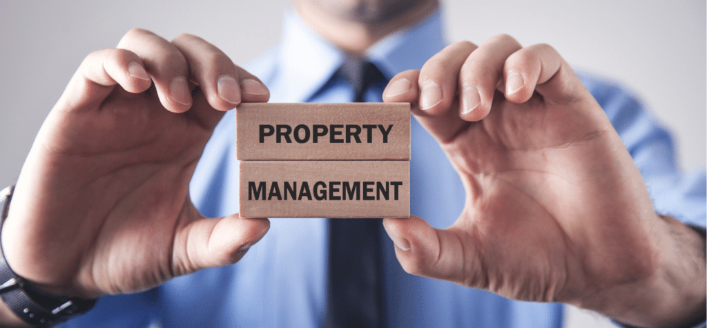 photo of a man holding a wood sign saying property management showing how to create wealth investing in real estate